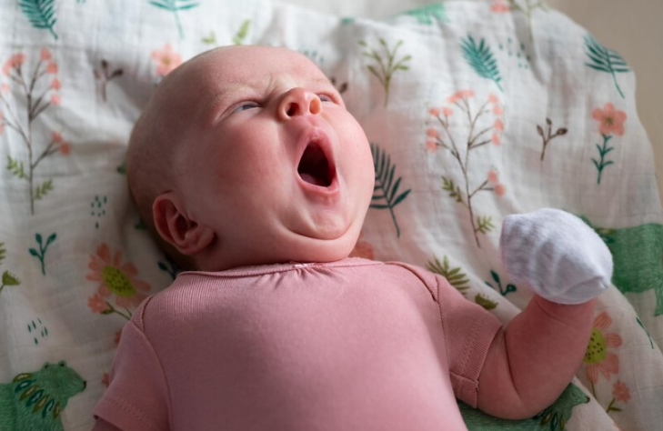 baby yawning and wearing mittens
